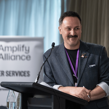 A speaker presenting at an Amplify Alliance event from a podium.